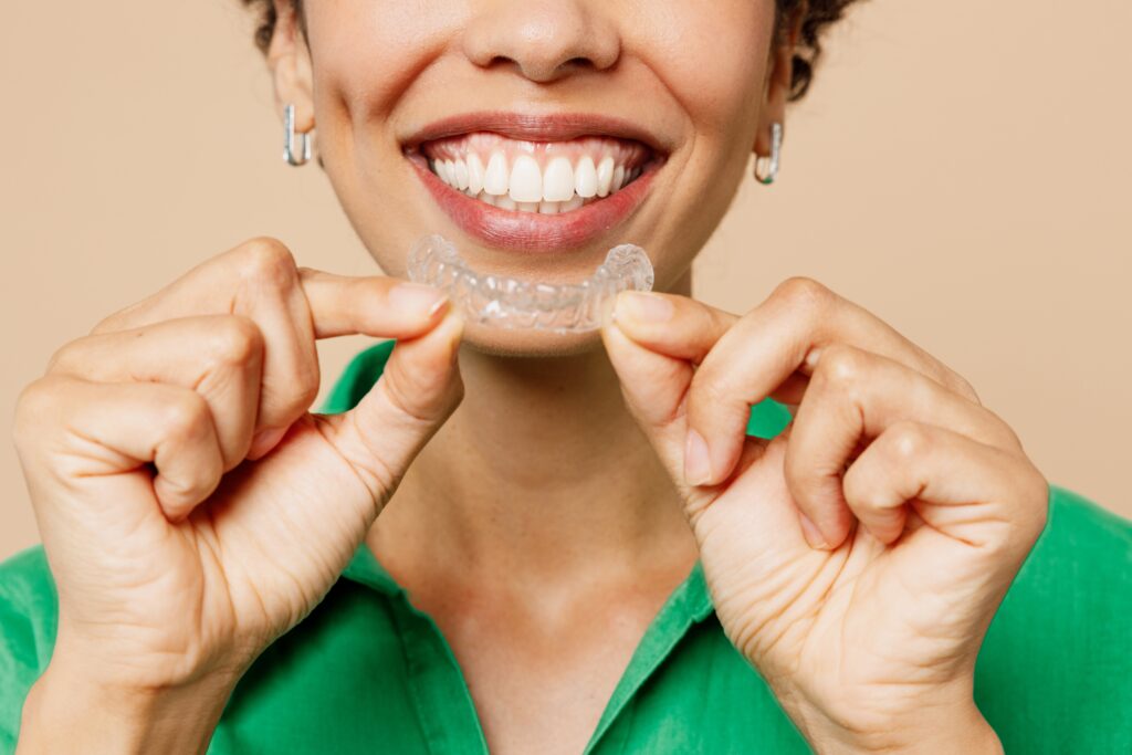 Close up of a smiling woman with straight teeth putting on her Invisalign aligners