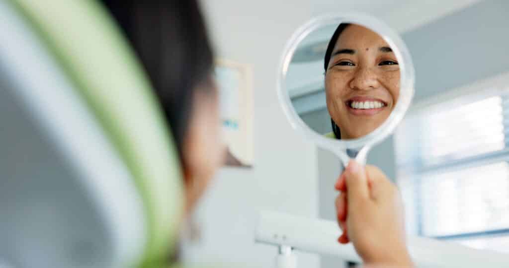 Woman smiling and looking at herself in the mirror after her full mouth rejuvenation dental treatment