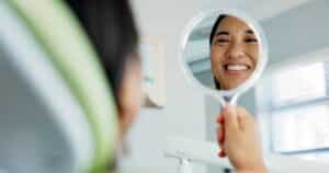 Woman smiling and looking at herself in the mirror after her full mouth rejuvenation dental treatment